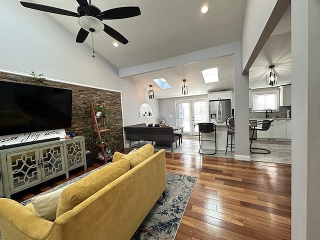 living room featuring french doors, lofted ceiling with skylight, light hardwood / wood-style floors, and ceiling fan