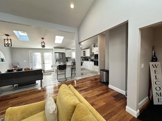 living room with hardwood / wood-style flooring, french doors, and vaulted ceiling with skylight