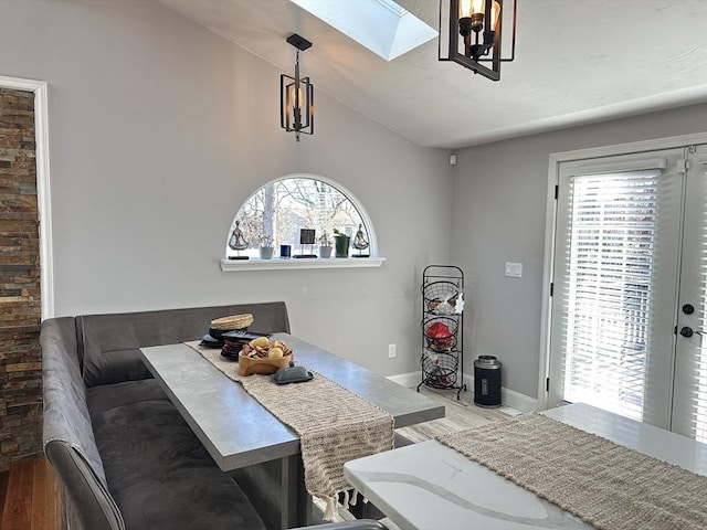 dining area with hardwood / wood-style flooring, vaulted ceiling with skylight, a chandelier, and breakfast area