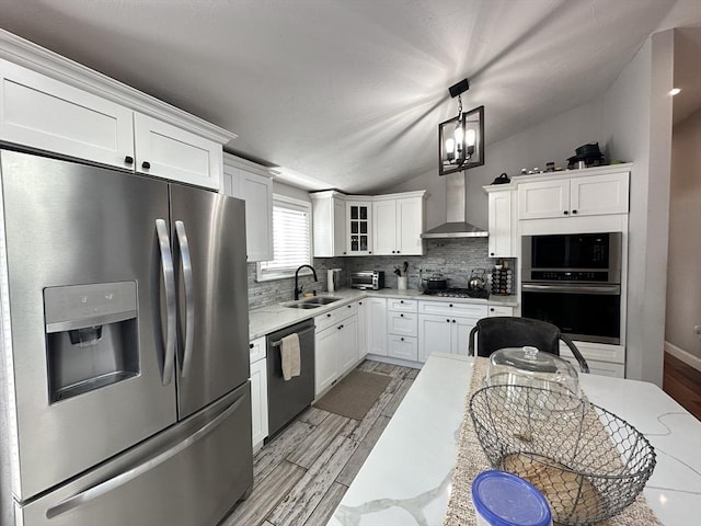 kitchen with pendant lighting, wall chimney range hood, lofted ceiling, white cabinetry, and appliances with stainless steel finishes