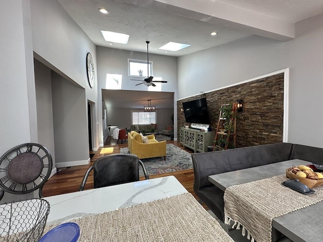 dining area with a towering ceiling, ceiling fan, a skylight, and dark hardwood / wood-style floors