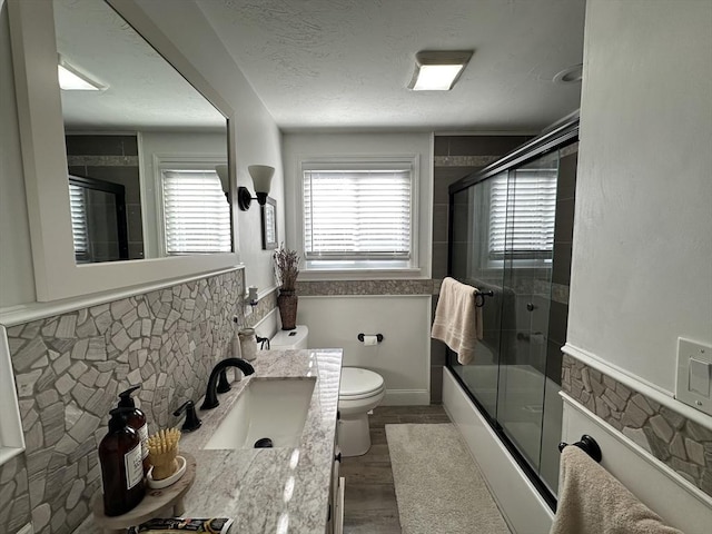 full bathroom featuring hardwood / wood-style floors, bath / shower combo with glass door, vanity, and toilet