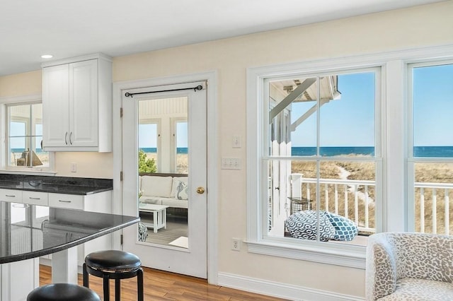 doorway with a water view, a wealth of natural light, wood finished floors, and baseboards