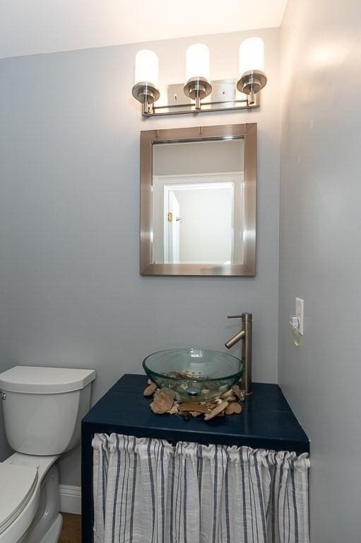 half bathroom featuring baseboards, toilet, and vanity