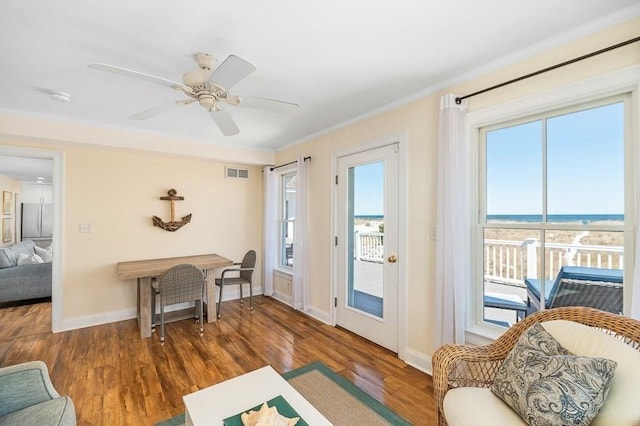 interior space with wood finished floors, a water view, baseboards, visible vents, and crown molding