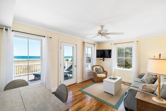 living area featuring ceiling fan, a water view, wood finished floors, and baseboards