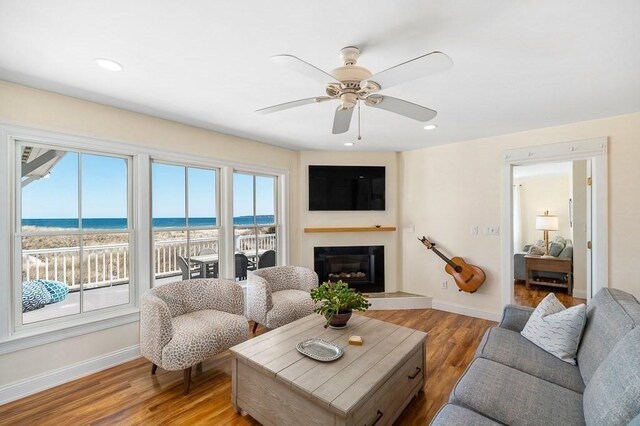 living area featuring a glass covered fireplace, ceiling fan, baseboards, and light wood-type flooring