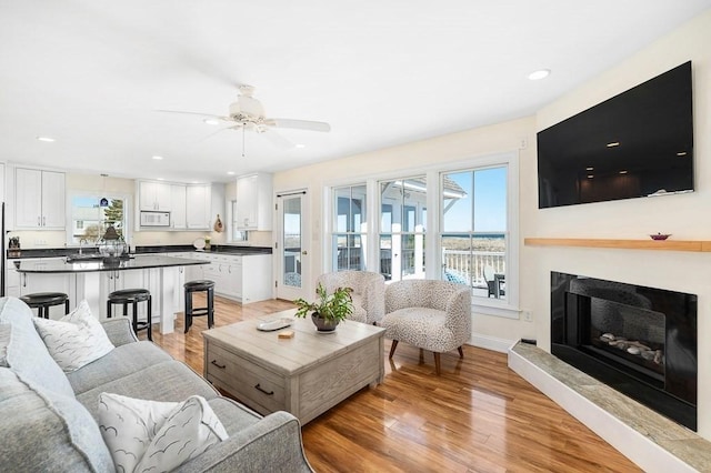 living area with recessed lighting, a glass covered fireplace, light wood-type flooring, a ceiling fan, and baseboards