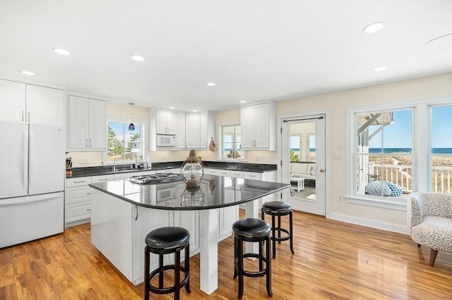 kitchen featuring a breakfast bar area, light wood finished floors, white cabinetry, and white appliances