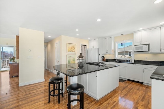 kitchen with wood finished floors, white appliances, a kitchen island, dark countertops, and a sink