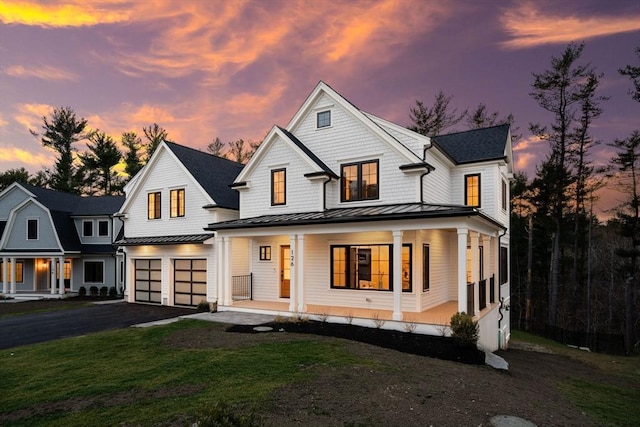 view of front of home with a front lawn, driveway, a standing seam roof, covered porch, and an attached garage