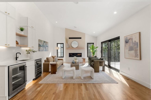 living room featuring wine cooler, light wood-style flooring, a fireplace, and high vaulted ceiling