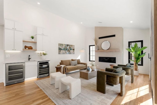 living room with wet bar, beverage cooler, light wood finished floors, and a large fireplace