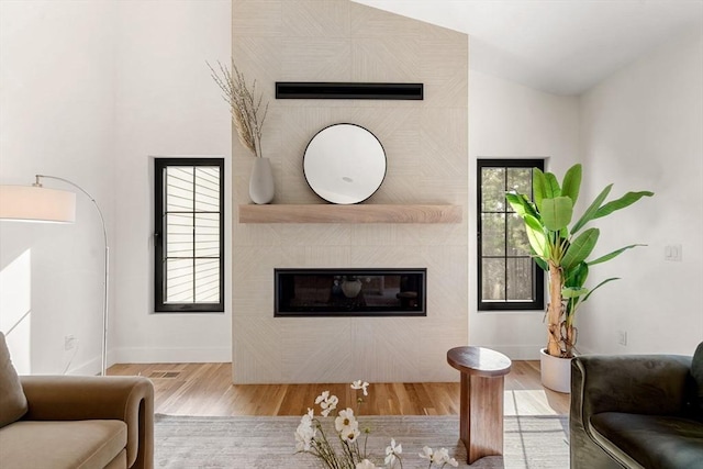 living area with baseboards, lofted ceiling, wood finished floors, and a tiled fireplace