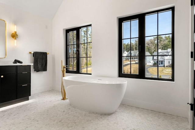 full bath with a soaking tub, vanity, baseboards, and vaulted ceiling