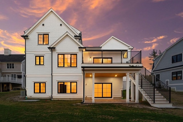 back of property at dusk with a patio area, stairs, and a yard