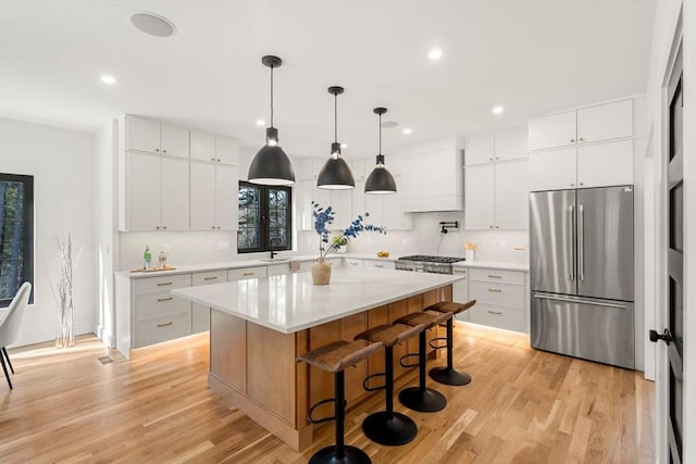 kitchen featuring premium range hood, light countertops, a kitchen breakfast bar, light wood-style floors, and stainless steel refrigerator