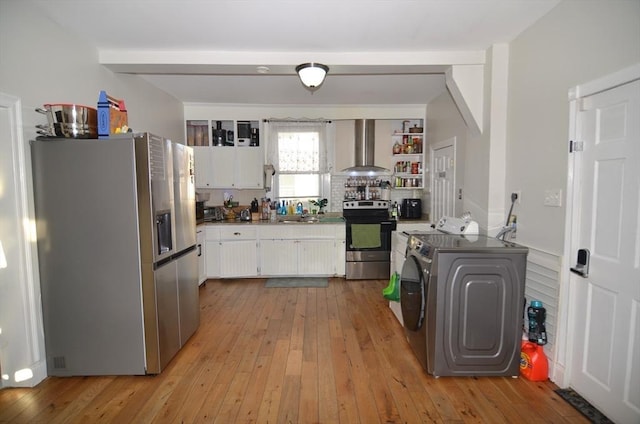 kitchen with stainless steel appliances, white cabinets, wall chimney exhaust hood, light hardwood / wood-style flooring, and washer and dryer