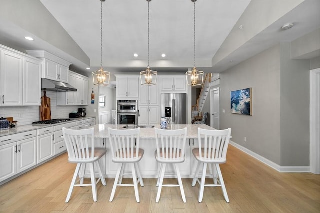 kitchen with under cabinet range hood, stainless steel appliances, vaulted ceiling, light wood-type flooring, and backsplash