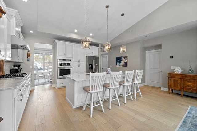 kitchen with light wood finished floors, a kitchen island with sink, appliances with stainless steel finishes, and white cabinetry