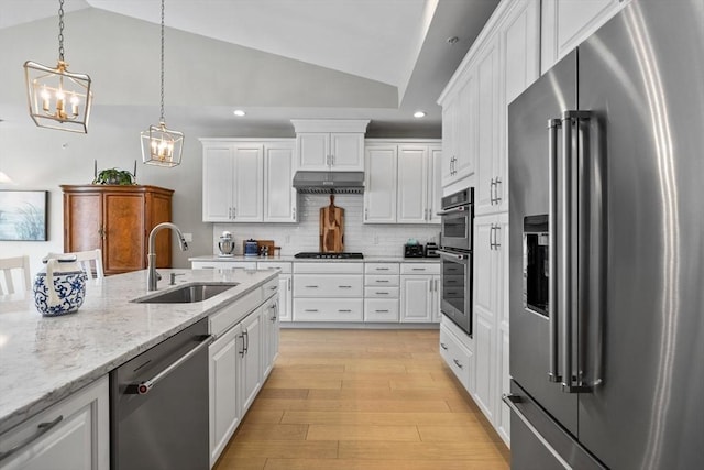 kitchen featuring light wood finished floors, lofted ceiling, stainless steel appliances, under cabinet range hood, and a sink