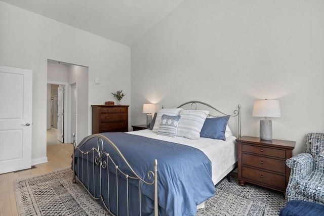 bedroom with vaulted ceiling, light wood-style flooring, and baseboards