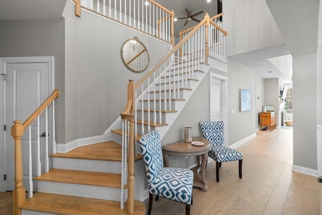 staircase featuring a towering ceiling, baseboards, and wood finished floors