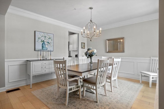 dining room with light wood finished floors, visible vents, a wainscoted wall, an inviting chandelier, and crown molding