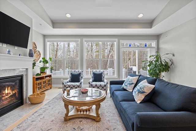 living room with a premium fireplace, a raised ceiling, and baseboards