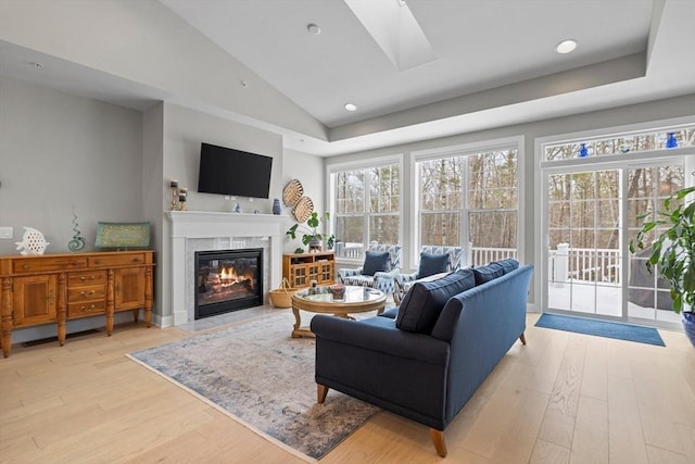 living room with lofted ceiling with skylight, light wood-type flooring, a glass covered fireplace, and recessed lighting