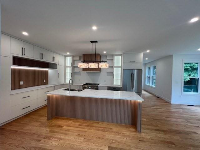 kitchen featuring stainless steel appliances, an island with sink, sink, and white cabinetry