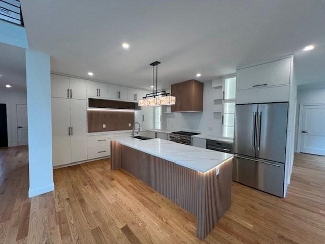 kitchen featuring sink, high end appliances, white cabinetry, decorative light fixtures, and a center island with sink