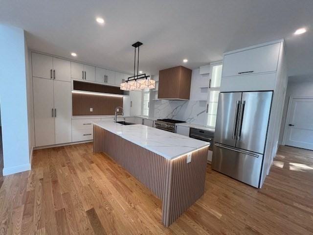 kitchen with white cabinetry, decorative light fixtures, light wood-type flooring, appliances with stainless steel finishes, and an island with sink