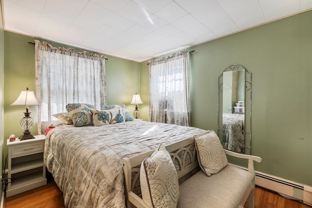 bedroom featuring a baseboard heating unit and wood-type flooring