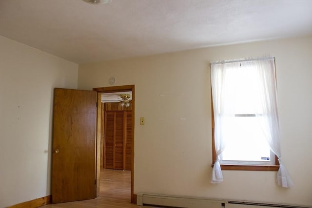 spare room with a baseboard heating unit, healthy amount of natural light, light wood finished floors, and ceiling fan