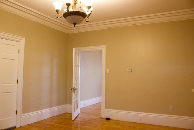 empty room with a chandelier, wood finished floors, crown molding, and baseboards