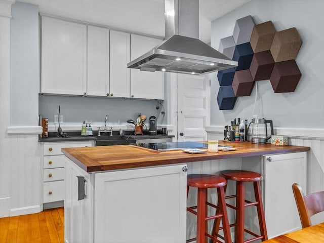 4 Greenough Ave, Boston, MA 02130 - kitchen with wall chimney exhaust hood, butcher block countertops, white cabinetry, a breakfast bar area, and a wainscoted wall
