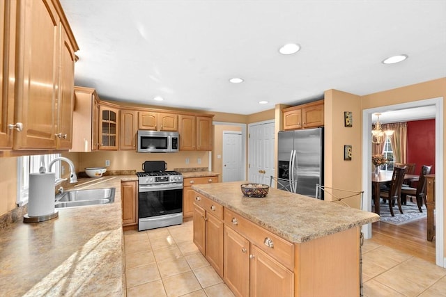 kitchen with sink, stainless steel appliances, a kitchen island, an inviting chandelier, and light tile patterned flooring