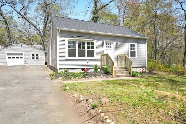bungalow-style home featuring driveway, roof with shingles, a detached garage, an outdoor structure, and a front lawn