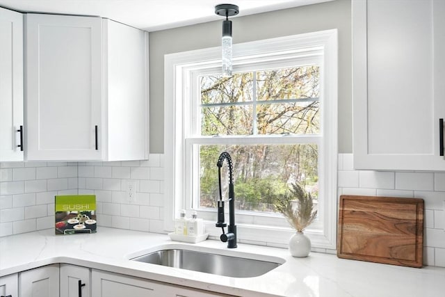 kitchen featuring white cabinets, light stone countertops, a sink, and tasteful backsplash