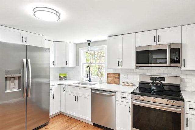 kitchen with white cabinets, a sink, light countertops, stainless steel appliances, and backsplash