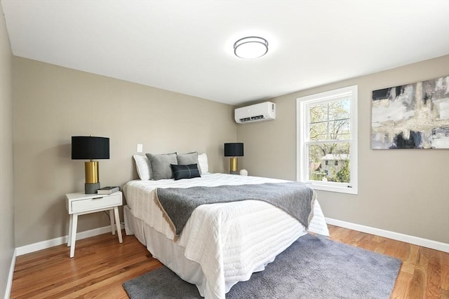 bedroom featuring wood finished floors, baseboards, and a wall unit AC
