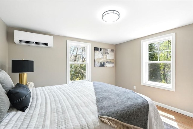 bedroom with baseboards, a wall mounted air conditioner, wood finished floors, and multiple windows