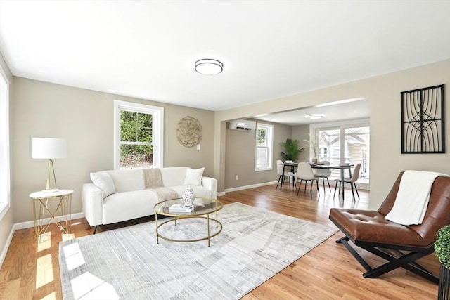living room with baseboards, a wall unit AC, and light wood-style flooring
