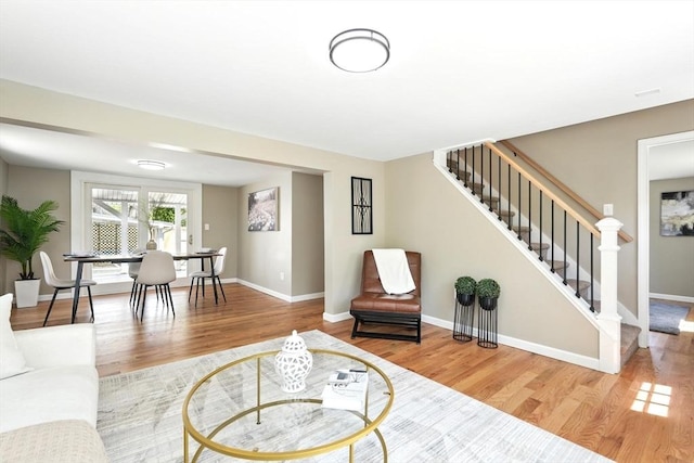living area with baseboards, wood finished floors, and stairway