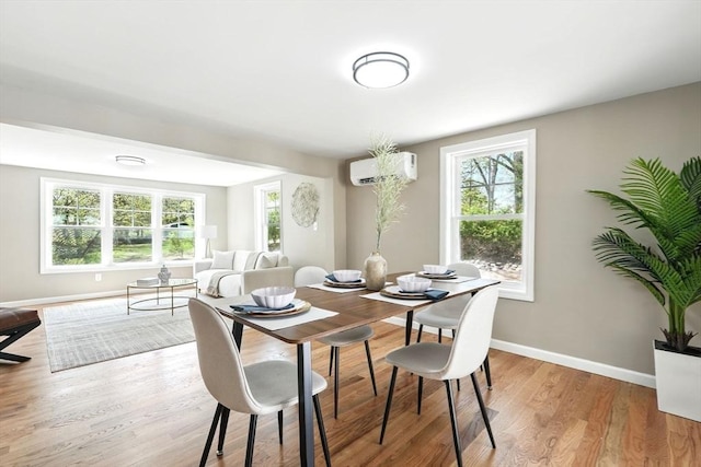 dining room with baseboards, a wall unit AC, and light wood finished floors