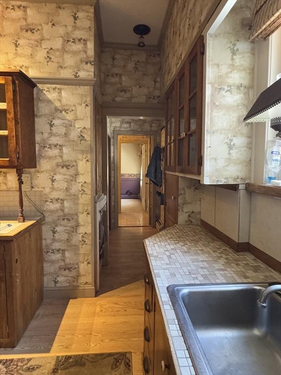 kitchen with light wood finished floors, glass insert cabinets, brown cabinetry, and a sink