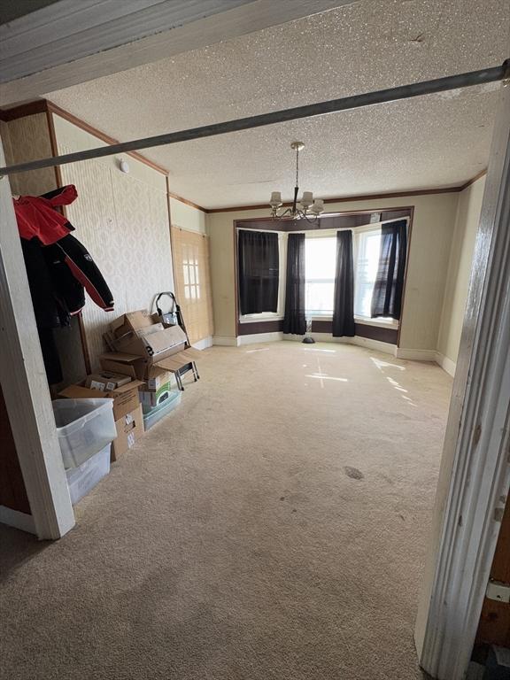 interior space featuring a textured ceiling, crown molding, carpet flooring, baseboards, and an inviting chandelier