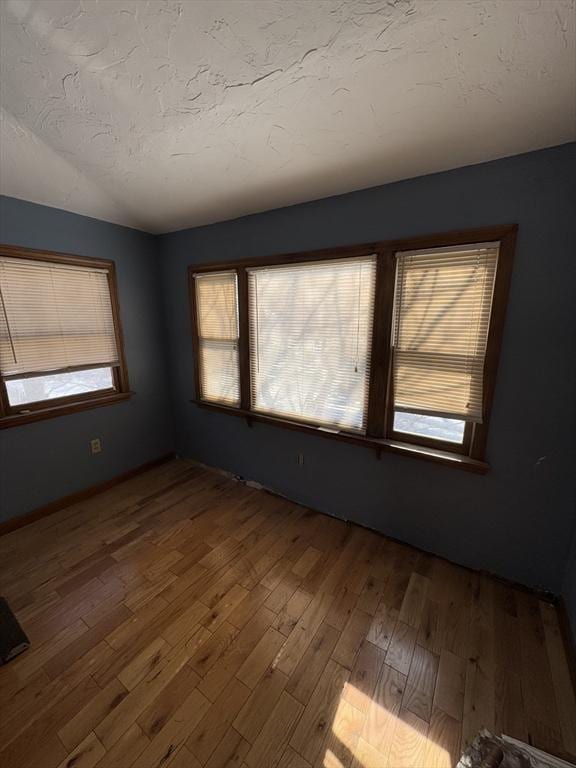 unfurnished room featuring wood-type flooring, a healthy amount of sunlight, and a textured ceiling