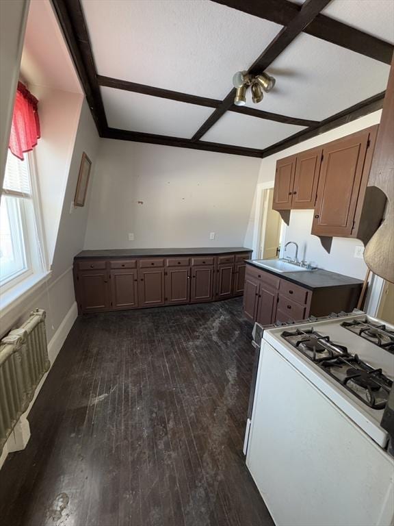 kitchen with gas range gas stove, radiator heating unit, dark wood-type flooring, a sink, and baseboards